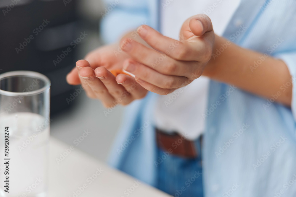 Woman's hands holding a pill in front of a glass of water, closeup view of medication and hydration concept