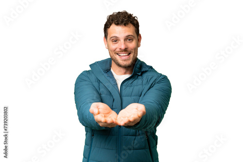 Brazilian man over isolated chroma key background holding copyspace imaginary on the palm to insert an ad