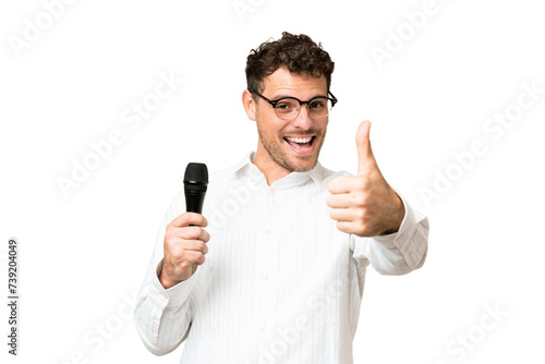 Brazilian man picking up a microphone over isolated chroma key background with thumbs up because something good has happened