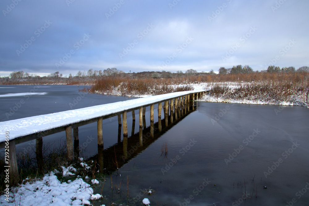 Obraz premium Snow-covered footbridge over the lake and the blue water