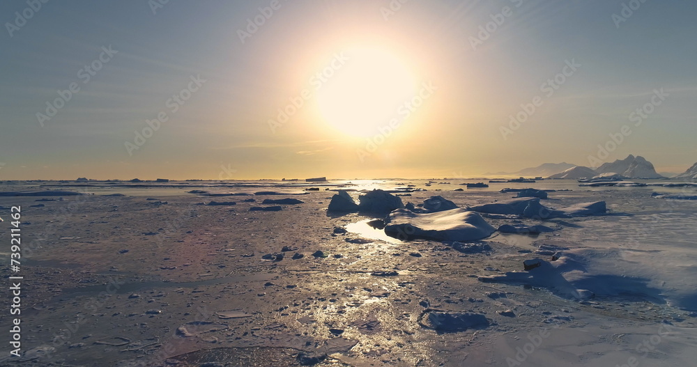 Fly over polar frozen ocean landscape in sunset. Serene beauty of glaciers surrounded by pristine icy snow land. Untouched wilderness of Antarctica. South Pole travel background. Low angle drone shot