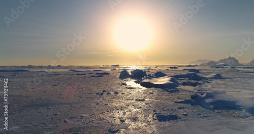 Fly over polar frozen ocean landscape in sunset. Serene beauty of glaciers surrounded by pristine icy snow land. Untouched wilderness of Antarctica. South Pole travel background. Low angle drone shot