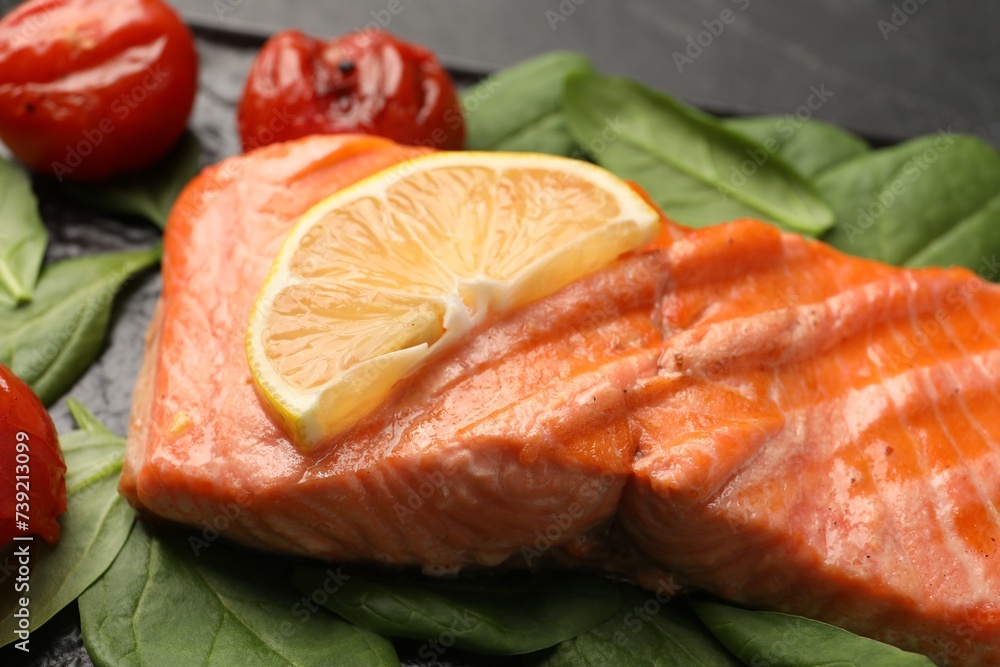 Tasty grilled salmon with tomatoes, lemon and spinach on table, closeup Tasty grilled salmon with tomatoes, lemon and spinach on table, closeup