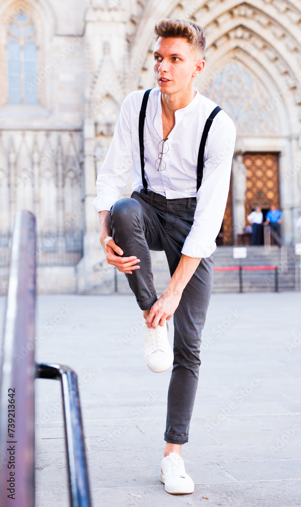 Young European guy in shirt and trousers with suspenders walking around city