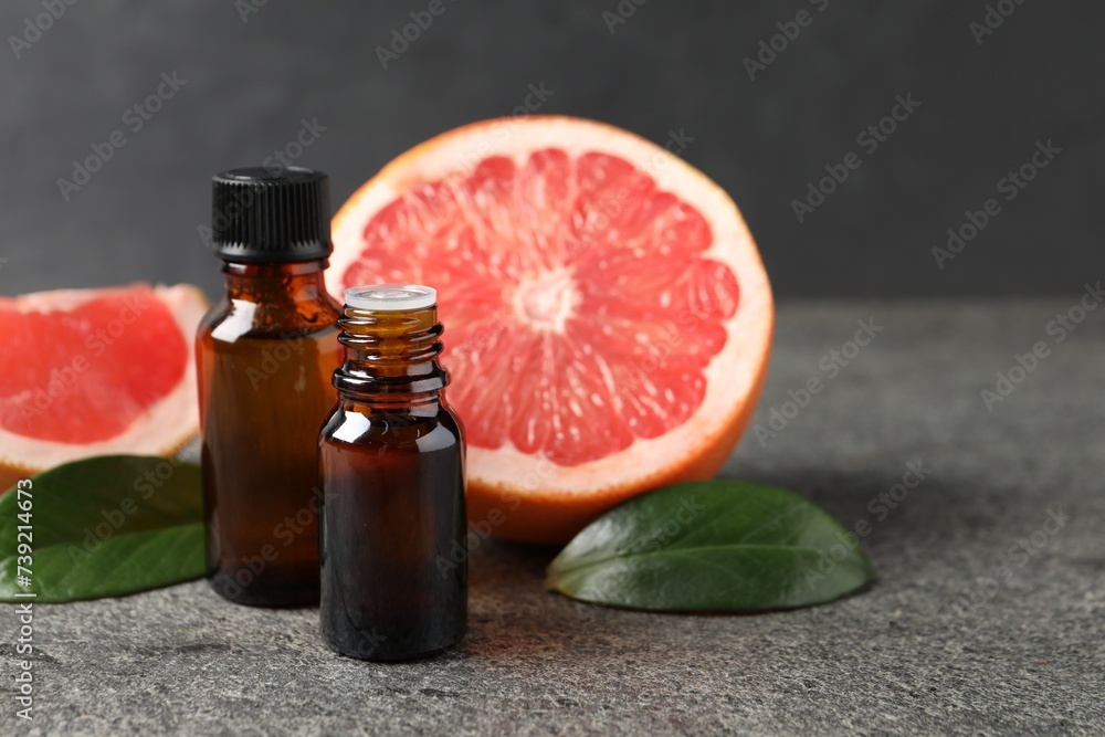 Grapefruit essential oil in bottles, leaves and fruits on dark textured table, closeup. Space for text Grapefruit essential oil in bottles, leaves and fruits on dark textured table, closeup. Space for text