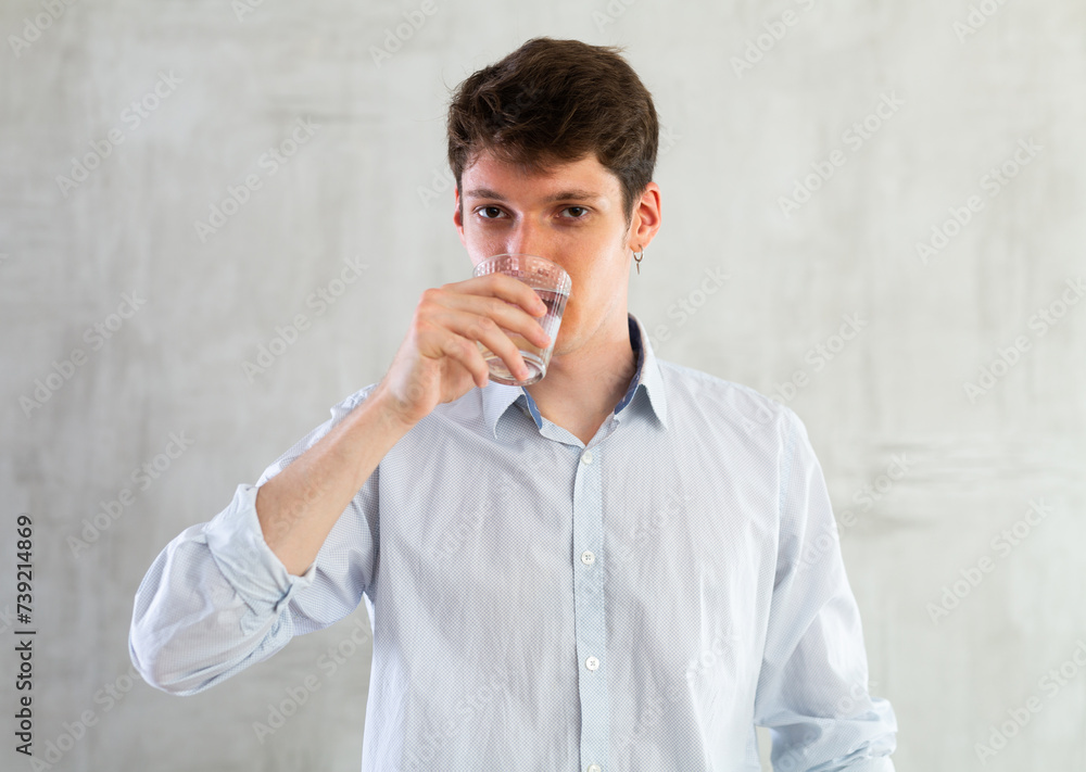 Positive young man drinking water from glass