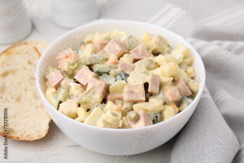 Tasty Olivier salad with boiled sausage in bowl and bread on white table, closeup