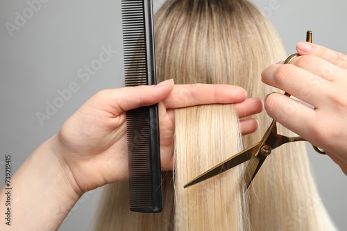 Hairdresser cutting client's hair with scissors on light grey background, closeup