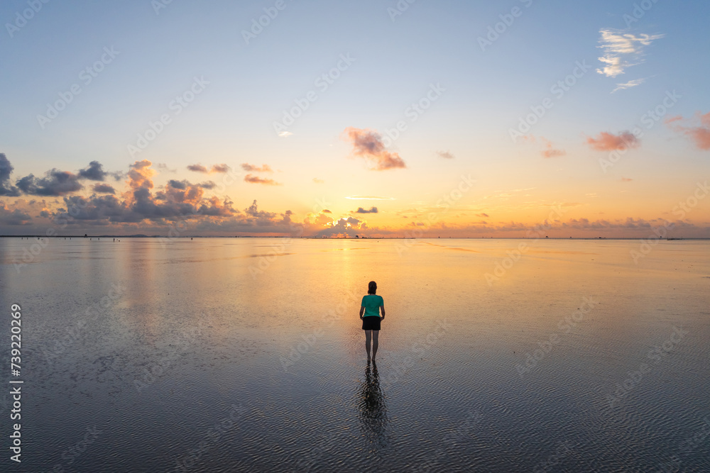  A female traveler standing on be beach in sunrise with reflection background