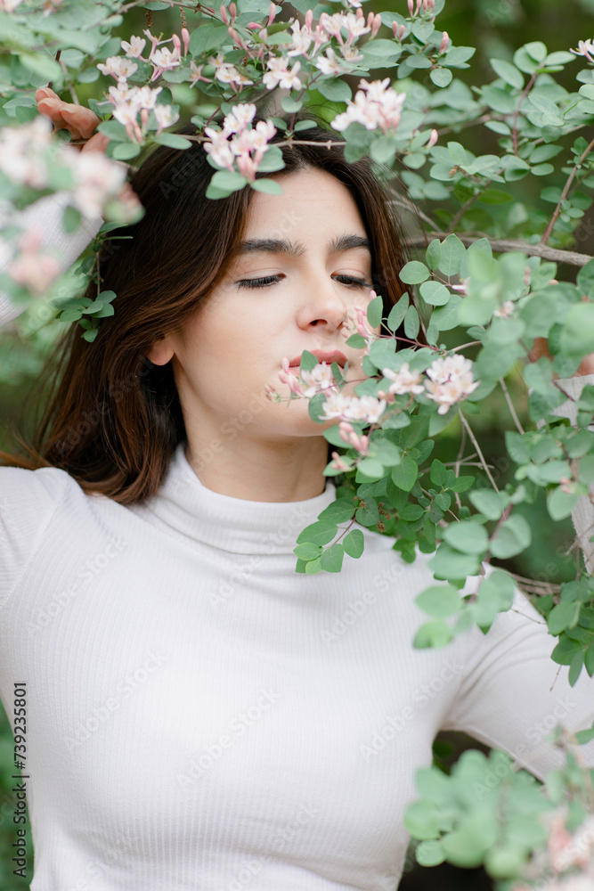 Close up of pretty, brunette girl having photoshoot in park, smelling tree branch, looking down. Concept of springtime.