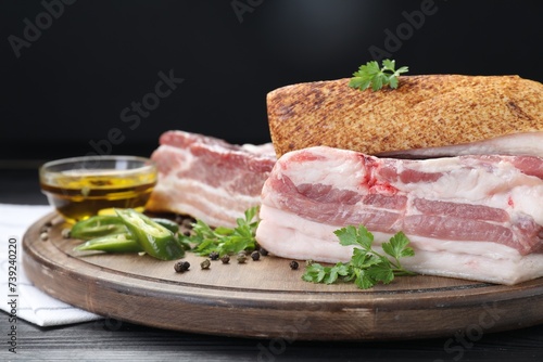 Pieces of raw pork belly  chili pepper  peppercorns  oil and parsley on black wooden table  closeup