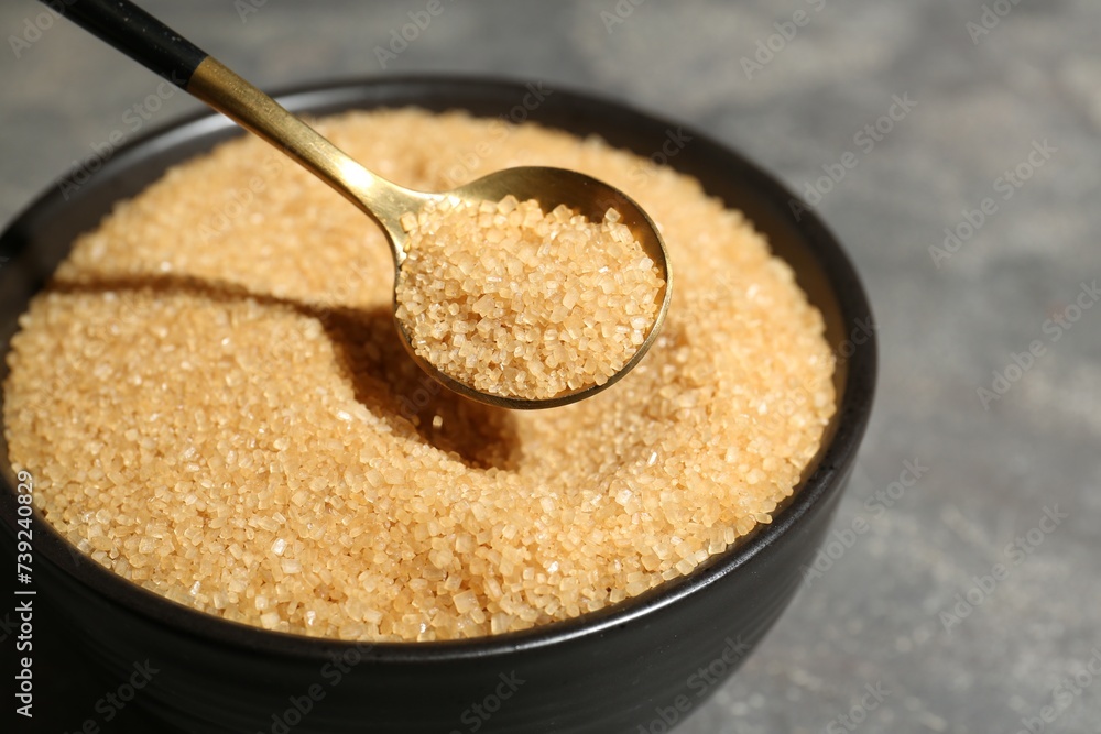 Taking brown sugar with spoon from bowl at grey table, closeup