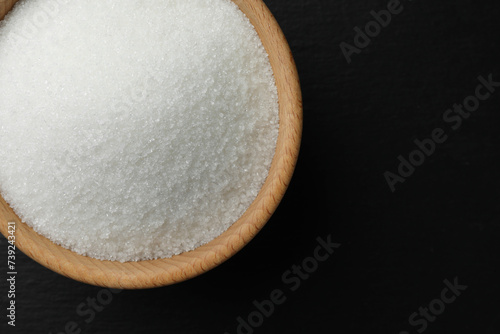 Granulated sugar in bowl on black table, top view. Space for text