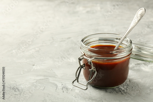 Tasty barbeque sauce in jar on grey textured table, closeup. Space for text