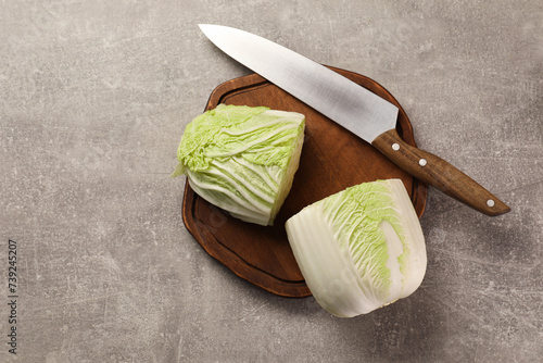Halves of fresh Chinese cabbage and knife on light grey table, top view