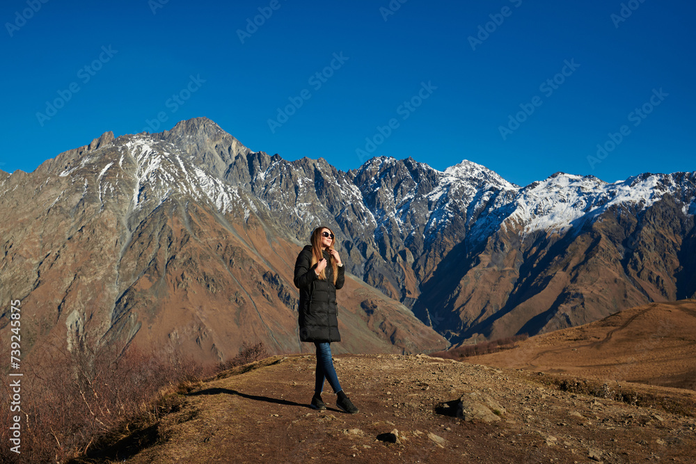 An adventurous traveler enjoying the magnificent view of the high brown mountains with snowy peaks.