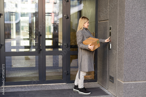 Happy woman ringing on doorbell at building entrance. Using intercom photo