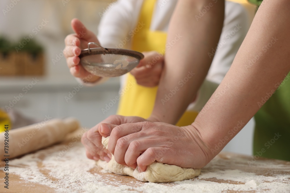 Fototapeta premium Making bread. Mother and her daughter kneading dough at wooden table in kitchen, closeup