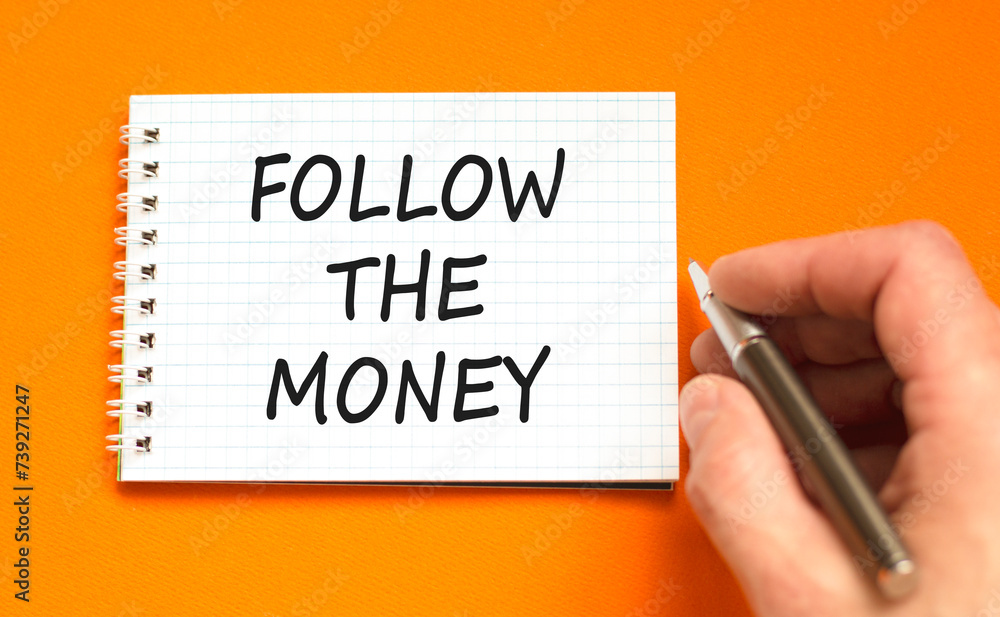 Follow the money symbol. Concept words Follow the money on beautiful white note. Beautiful orange background. Businessman hand. Business and follow the money concept. Copy space. Follow the money symbol. Concept words Follow the money on beautiful white note. Beautiful orange background. Businessman hand. Business and follow the money concept. Copy space.