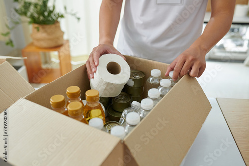 Volunteer putting food and necessities in cardboard box photo