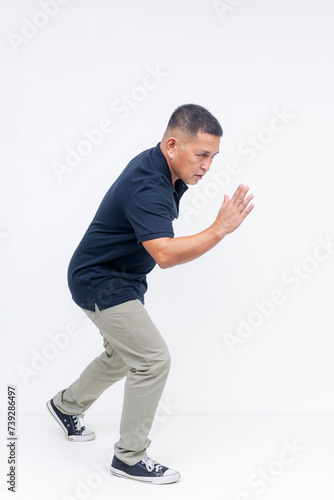 A focused middle aged Asian man in athletic pose, ready to sprint, isolated on a white background in full body shot.