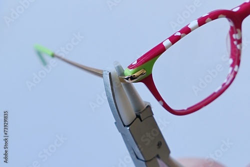 Adjusting inclination on patchy red and white children eyeglass frame with conical nylon jaws inclination pliers.