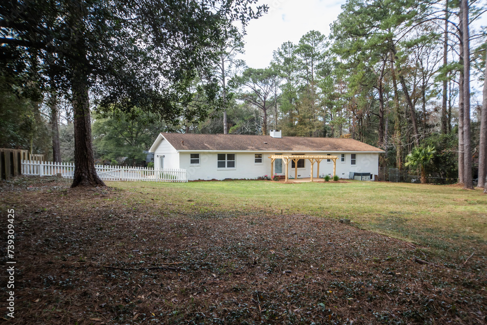 The rear back exterior of a newly painted and renovated white brick ranch style house with a large yard and a newly built wood arbor pergola for shade The rear back exterior of a newly painted and renovated white brick ranch style house with a large yard and a newly built wood arbor pergola for shade
