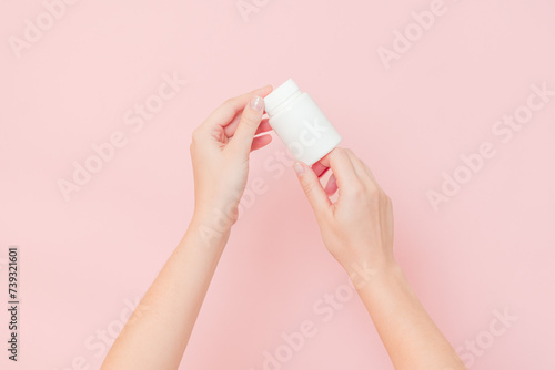 View on white bottle plastic tube in hands on pink background. Packaging for pills, capsules, supplements or ointment. Cosmetics