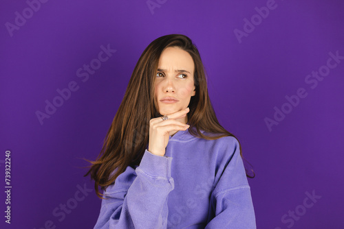 Portrait of minded brunette woman touch hand chin look at side think thoughts plan wear purple hoody isolated over violet color background.