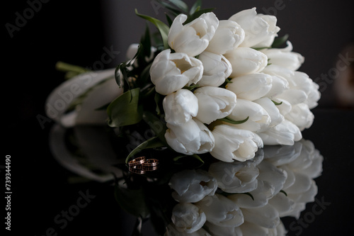Wedding bouquet of tulips on a black mirror table with wedding rings