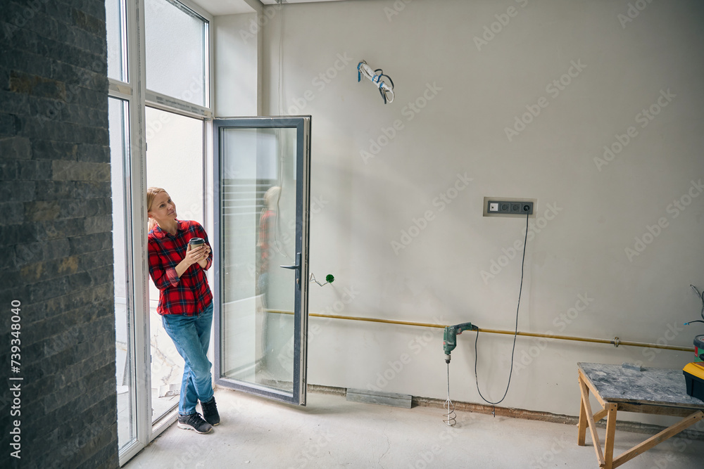 Workwoman stands near door and drinking coffee from paper glass