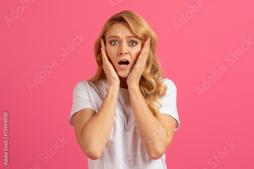 Young emotional blonde woman holding her face in shock, studio