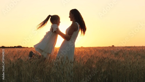 Happy family mother and daughter silhouette playing with love rotation at sunset sunrise wheat field closeup. Young woman and little girl kid turning around together at dusk dawn sun light meadow