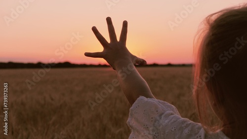 Cute little girl silhouette with hand shadow at bright sun sunset sunrise autumn wheat field closeup back view. Female kid child waving arm trying touching sunny cinematic sky meadow forest horizon