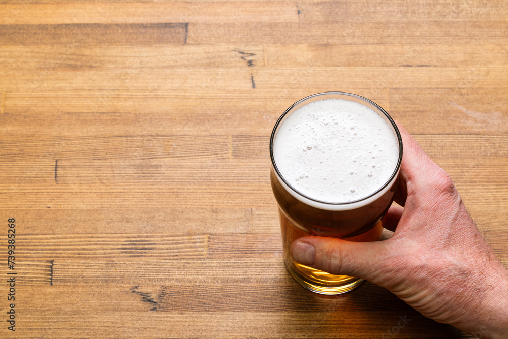 Hand Holding a Pint of Craft Beer on Wooden Table - obrazy, fototapety, plakaty 