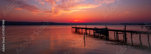 Stunning view of exciting red sunset at the shore with a wooden pier and moored boat