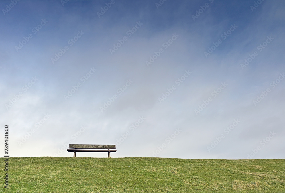 Eine Bank steht einsam auf einer Deichkrone unter blauem Februarhimmel Eine Bank steht einsam auf einer Deichkrone unter blauem Februarhimmel