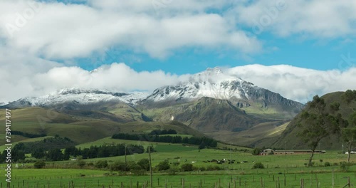 Time-lapse of Los Illiniza volcanic mountain over green fields with grazing cows on a sunny day photo