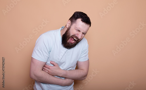 A man touching his stomach on beige background with copy space. Stomach pain and others stomach disease concept.