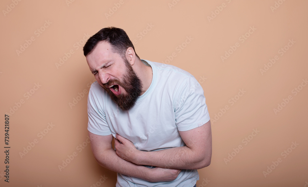 A man touching his stomach on beige background with copy space. Stomach pain and others stomach disease concept. A man touching his stomach on beige background with copy space. Stomach pain and others stomach disease concept.