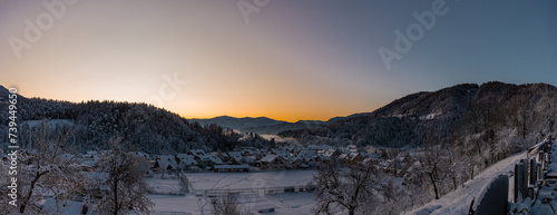 Panorama of houses covered with snow in the beautiful village of Ljubno ob Savinji, home of female ski jumping. Early morning with sun just about to rise, yellow skies, white covered forests. photo