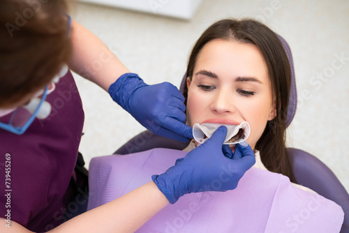 Orthodontist inserts a retractor into the mouth of the patient.  photo