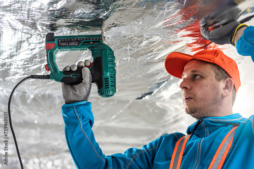 The builder is fastening the vapor barrier under the ceiling thermal insulation using an electric stapler.  The vapor barrier as protection of thermal insulation against internal moisture. photo