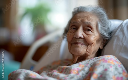 An elderly woman lies in a hospital bed, with tubes and medical equipment surrounding her. She gazes directly at the camera, showing a sense of resilience and strength amidst her medical condition.