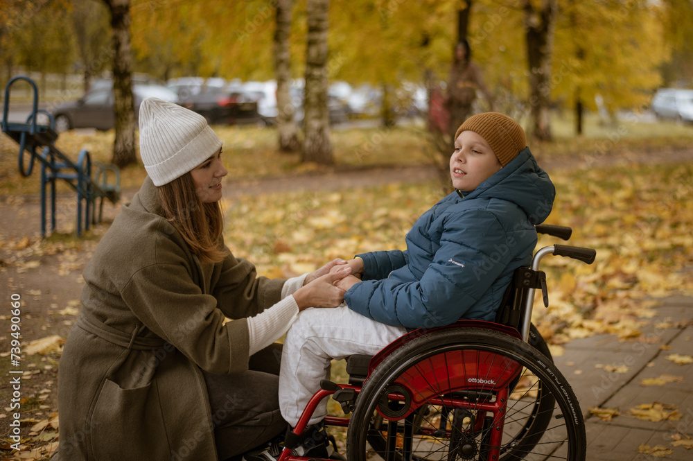 a 10-year-old boy in a wheelchair walks in the fall with his mother on the street with a dog on the playground. High quality photo