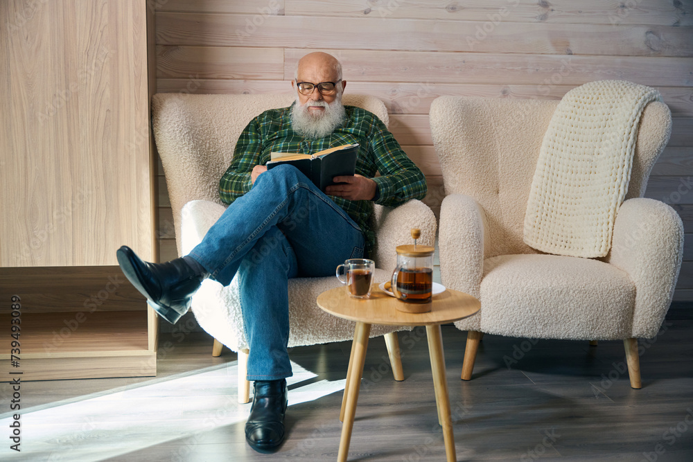 Old man sits comfortably with a book in a comfortable chair