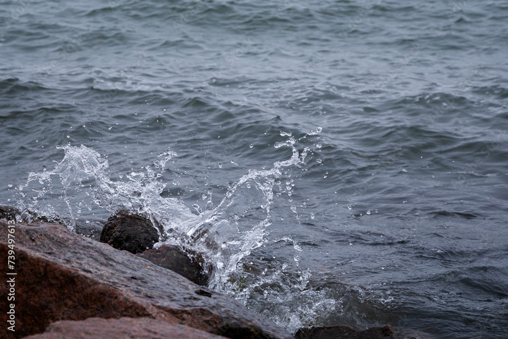 Close-up of splash of a small wave crashing on rocks.