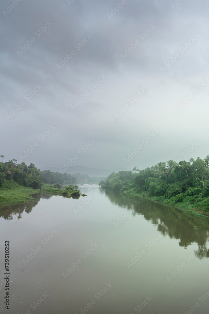 A landscape view of a calm river with green trees and mountain in India