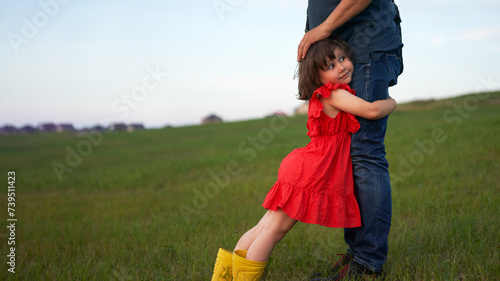 Nature vacation. A little girl embraced with her arms around the male relative's legs. Man stroking the child's head. Copy space.