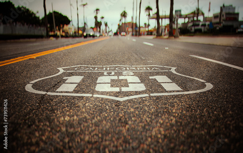 Highway 101 sign painted on the black asphalt road with city diffused in the background. The shot has vintage tones and is from Oceanside California